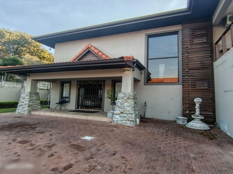 Front elevation of a townhouse featuring a paved driveway, stone-clad pillars, and a covered entrance with security gate.