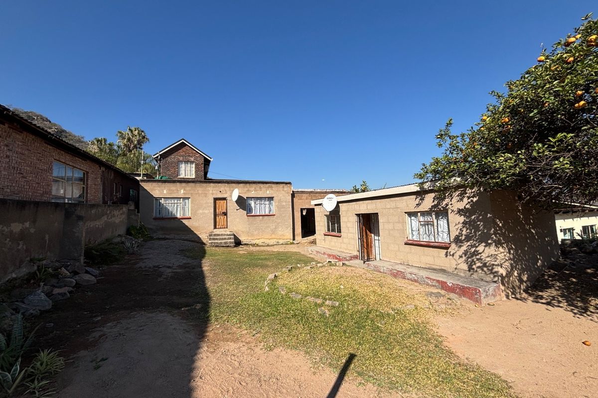 Rear view of the property showing multiple building sections, a central courtyard area, and established garden features under a clear sky.
