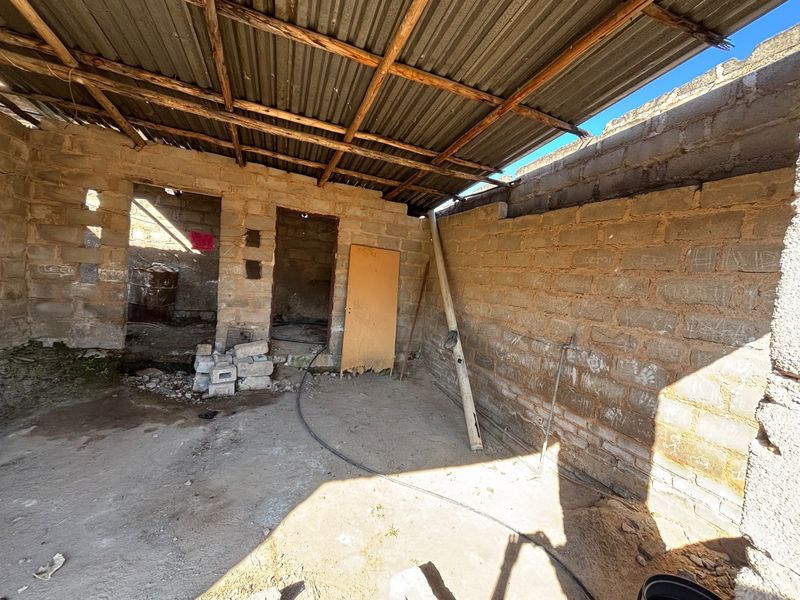 An unfinished utility space featuring exposed brick walls and a corrugated metal roof, requiring significant renovation and completion of structural finishes.