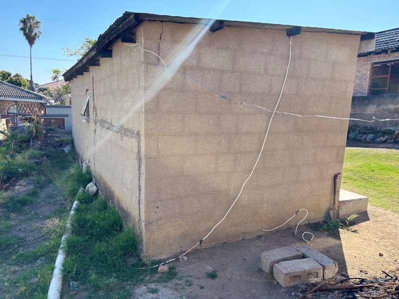 Rear view of an exterior structure showing exposed electrical wiring and significant wear on the concrete block walls and roof.