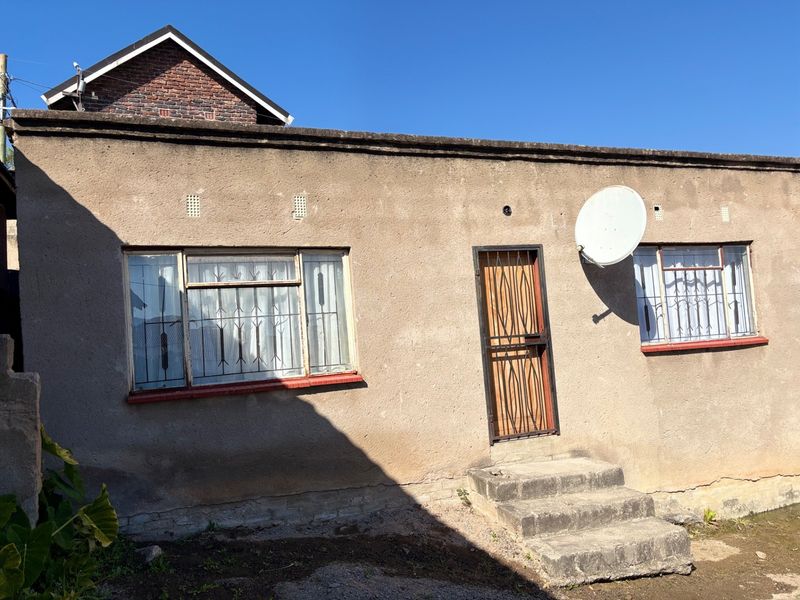 Rear exterior view of the property featuring plastered masonry walls, steel-framed windows with security bars, and concrete entrance steps.