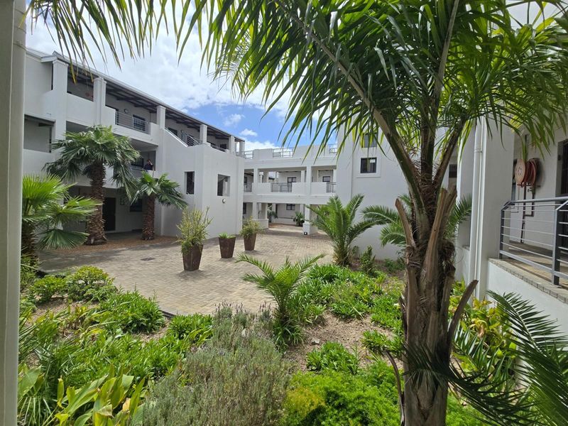 A well-maintained apartment complex courtyard featuring paved walkways, landscaped garden beds, and multi-level building access with modern balustrades.