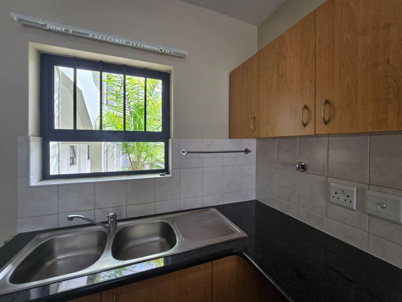 A functional kitchen area featuring wood-finish cabinetry, dark granite countertops, a double stainless steel sink, and tiled backsplash with window security bars.