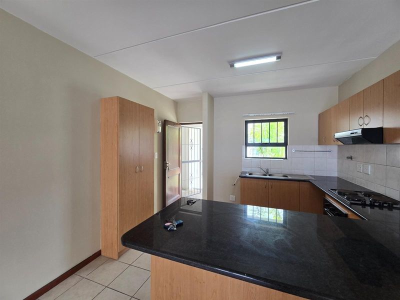 A functional kitchen featuring granite countertops, built-in cabinetry, integrated oven and hob, and tiled flooring with direct access to an exterior security gate.
