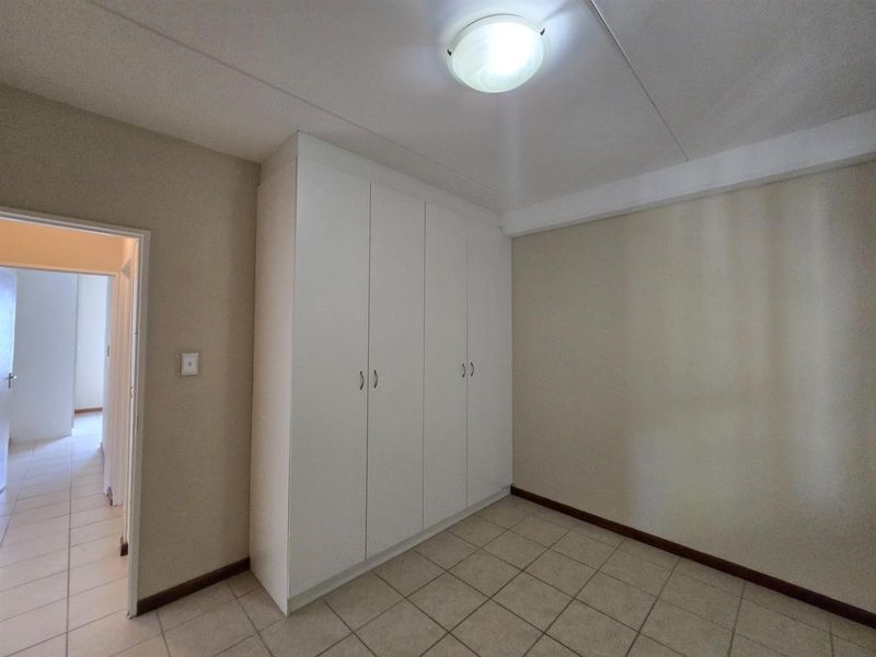 A clean, empty bedroom featuring neutral walls, tiled flooring, and built-in white cupboards, offering a versatile space ready for personalization.