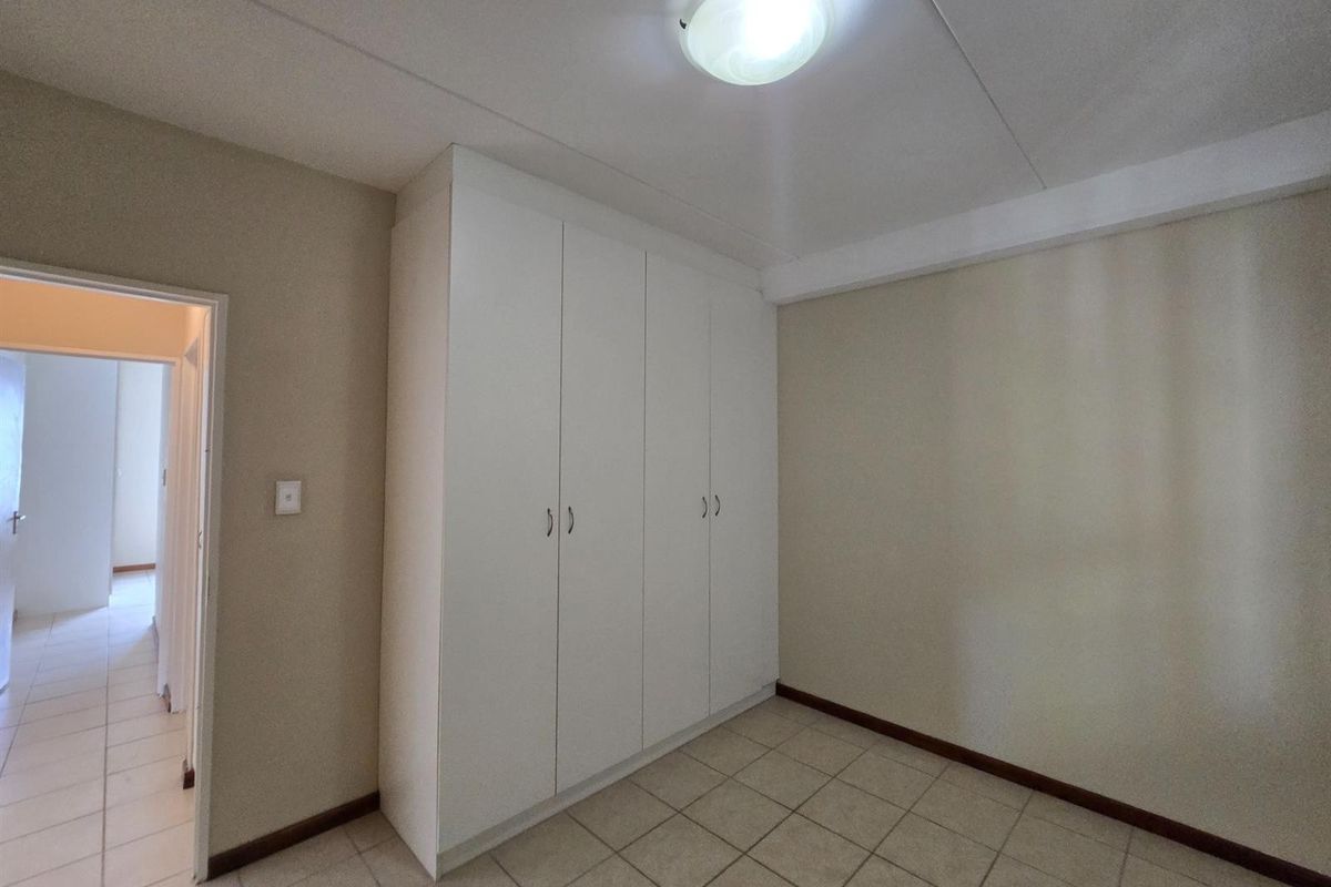 A clean, empty bedroom featuring neutral walls, tiled flooring, and built-in white cupboards, offering a versatile space ready for personalization.