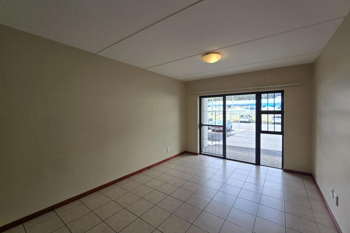 An empty, well-lit living room featuring neutral tiled flooring and a sliding glass door with integrated security gate providing access to the exterior.