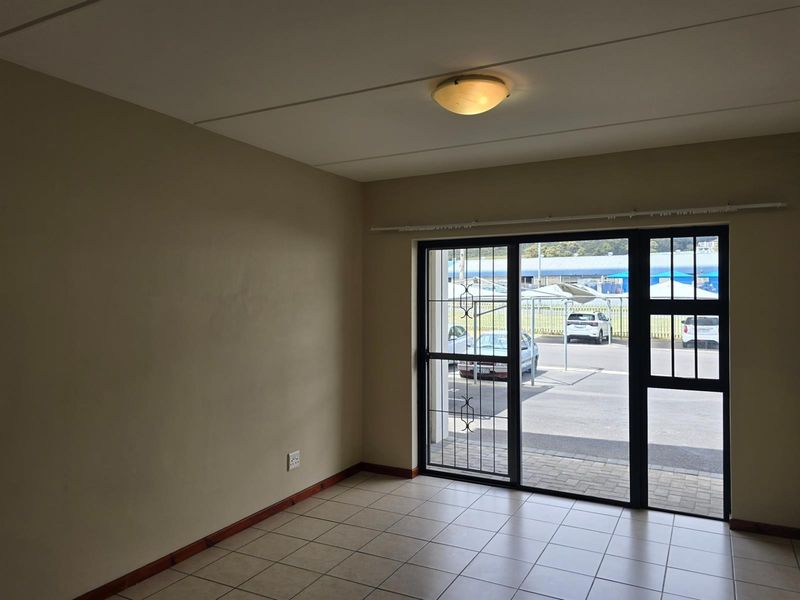 An empty living area featuring neutral walls, tiled flooring, and a sliding glass door with security gate providing access to the exterior.