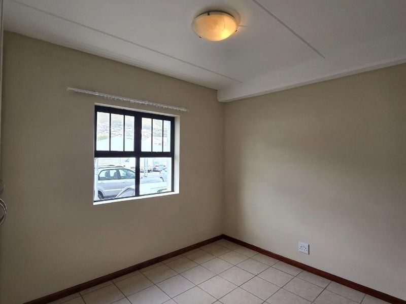 A clean, empty bedroom featuring neutral wall paint, tiled flooring, and a window with a dark frame.