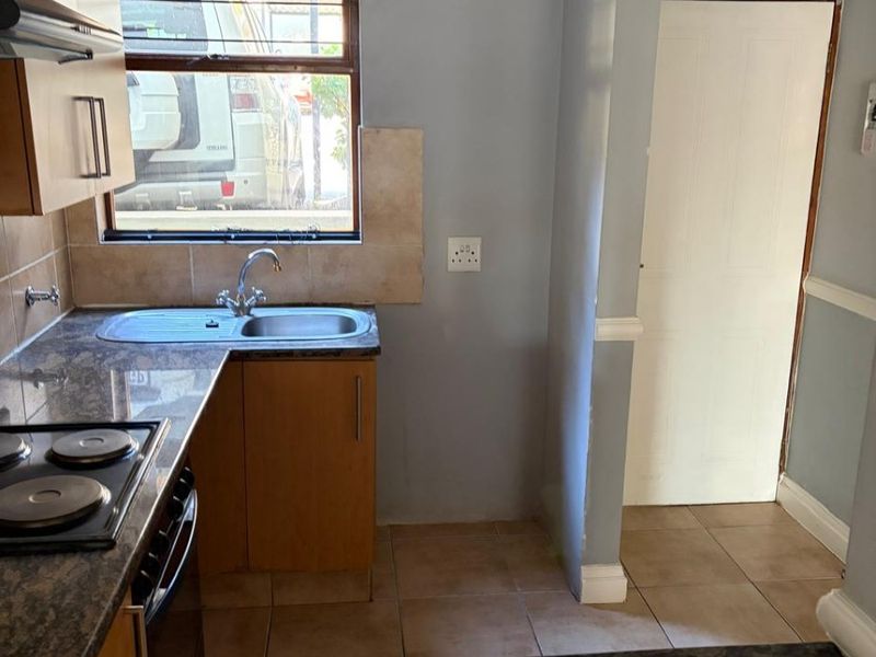 Compact kitchen featuring granite countertops, electric hob, extractor fan, and tiled flooring. The space offers functional cabinetry and a neutral layout.