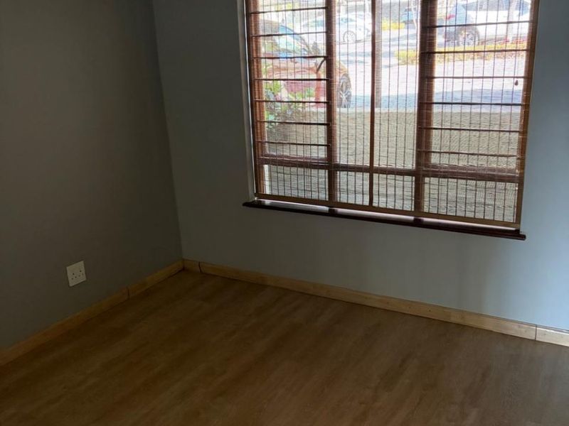 An empty bedroom featuring laminate flooring, neutral grey walls, and a window fitted with security bars and timber blinds.