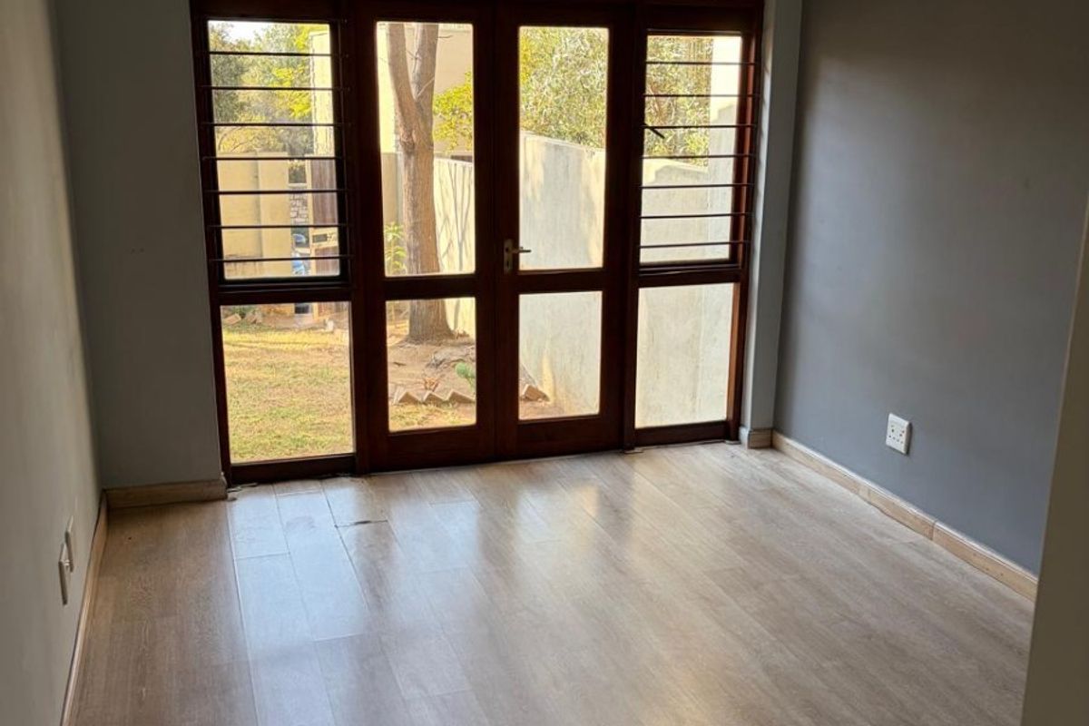 An empty bedroom featuring light-toned laminate flooring, grey walls, and wooden-framed glass doors providing access to the exterior.