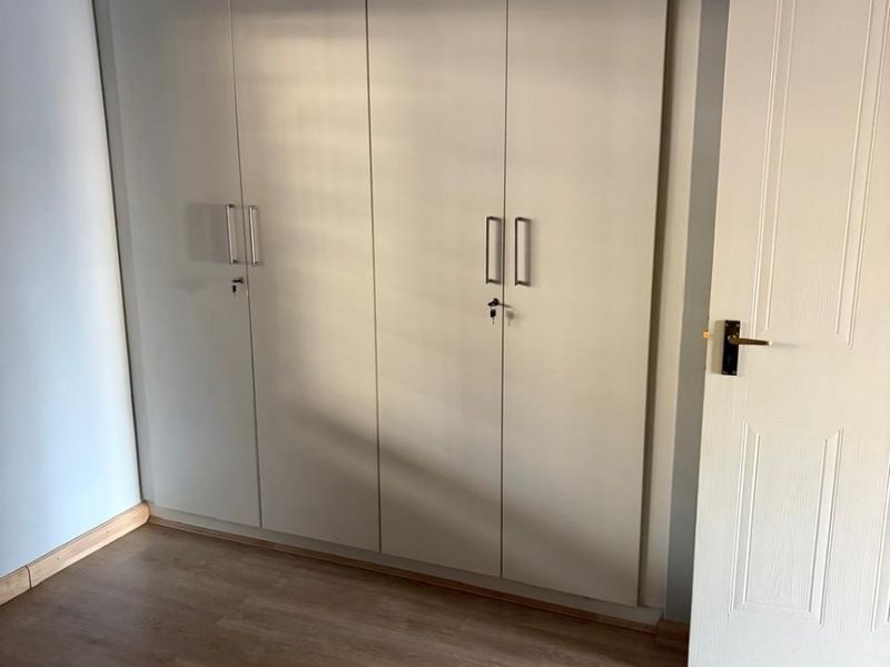 A clean, empty bedroom featuring light-toned laminate flooring and a large, floor-to-ceiling built-in wardrobe with modern handles.