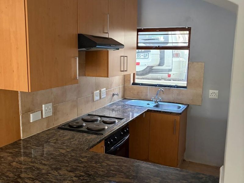 A compact kitchen featuring laminate cabinetry, granite countertops, a built-in electric hob, oven, and a stainless steel sink with a tiled backsplash.