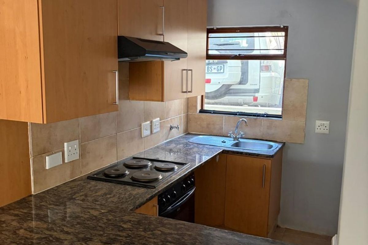 A compact kitchen featuring laminate cabinetry, granite countertops, a built-in electric hob, oven, and a stainless steel sink with a tiled backsplash.