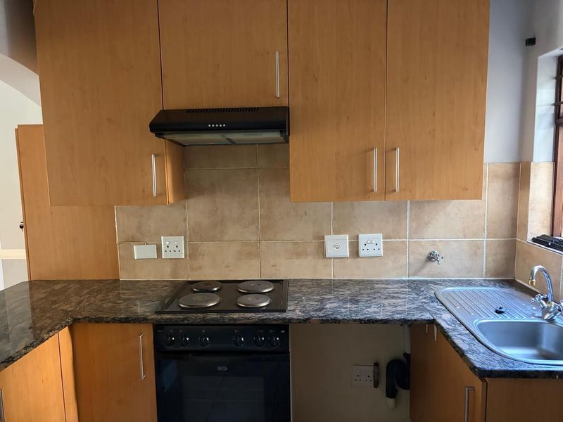 A functional kitchen featuring laminate cabinetry, granite countertops, a built-in oven with hob, and a stainless steel sink with tiled backsplash.