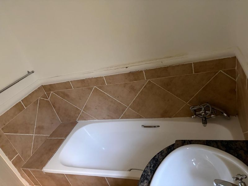 A bathroom featuring a built-in bathtub with tiled surround and a vanity basin with a granite countertop.
