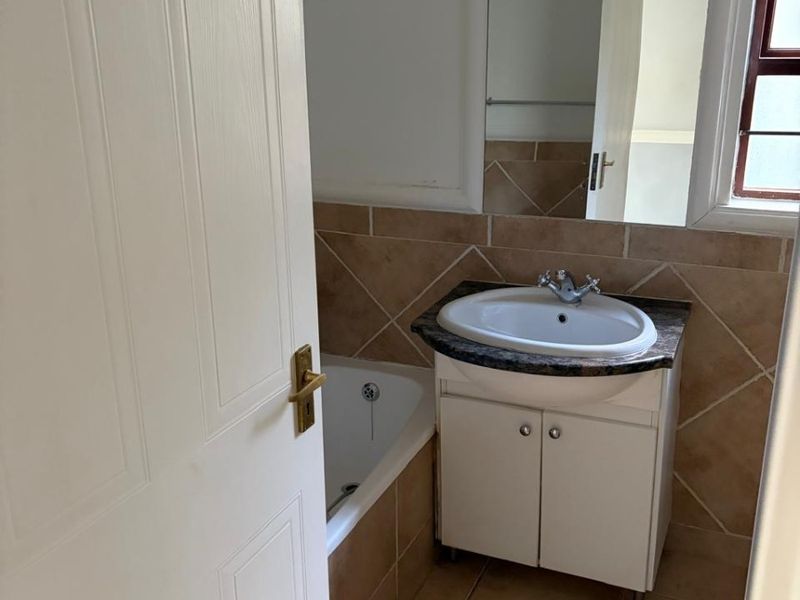 A functional bathroom featuring a vanity with basin, a bathtub, tiled flooring, and neutral wall tiling, offering a clean and practical space.