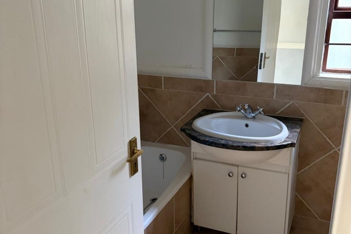 A functional bathroom featuring a vanity with basin, a bathtub, tiled flooring, and neutral wall tiling, offering a clean and practical space.