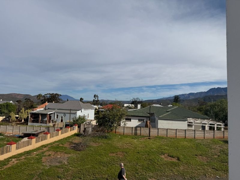 Elevated view overlooking a residential neighborhood with surrounding mountain scenery and a large open garden area.