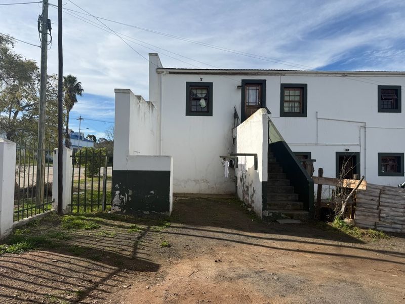 Rear exterior view of a white-painted building featuring an external staircase, metal security gate, and weathered masonry finishes.