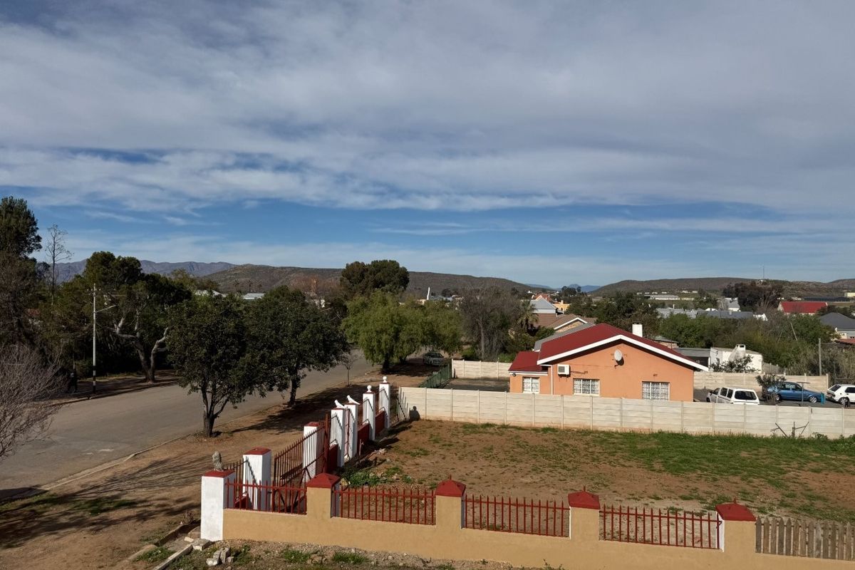 An elevated view of the property showing the surrounding neighborhood, perimeter fencing, and the main house structure with a tiled roof.