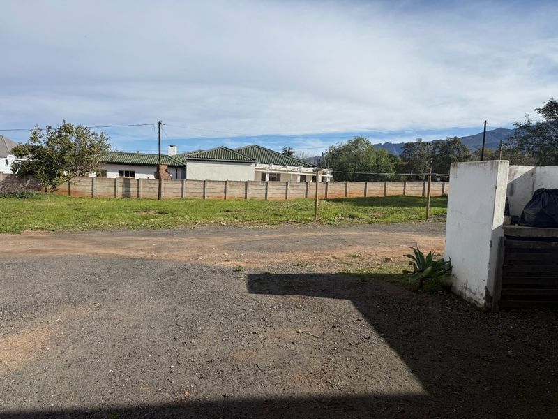 Rear exterior view of the property featuring a gravel driveway, open yard space, and a precast concrete boundary wall.