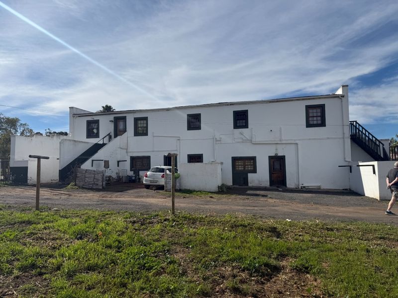 Rear elevation of a multi-level white plastered building featuring external staircases and timber-framed windows, set against a gravel yard area.