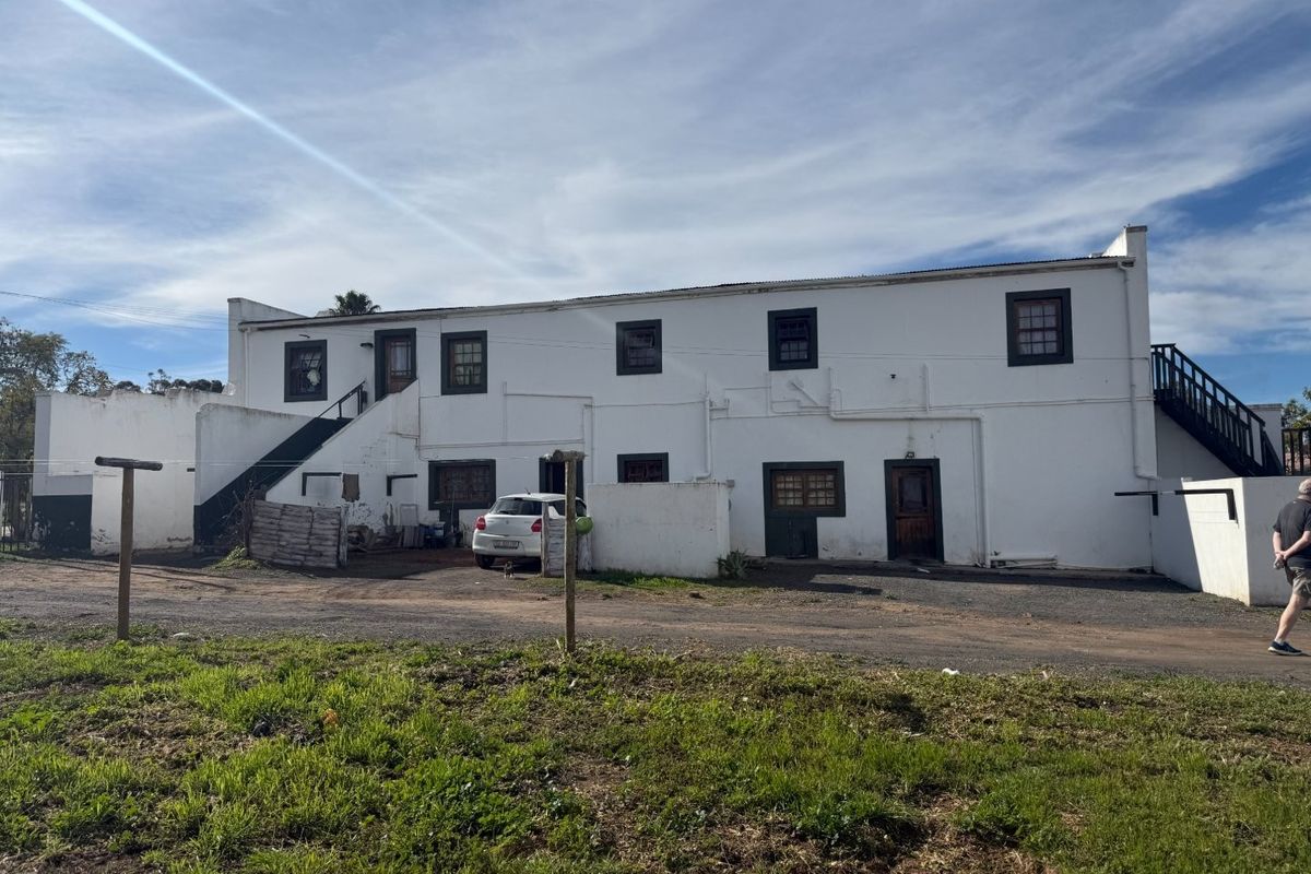 Rear elevation of a multi-level white plastered building featuring external staircases and timber-framed windows, set against a gravel yard area.