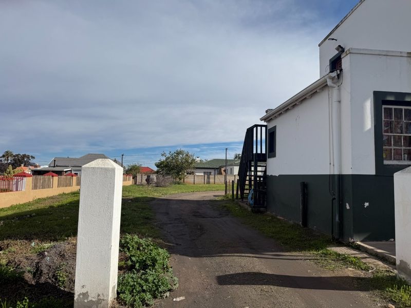 Rear view of the property showing an external staircase, unpaved driveway, and boundary walling with visible exterior maintenance required.