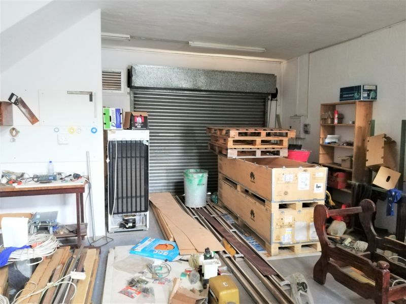 A functional commercial garage space featuring a secure roller shutter door, overhead strip lighting, and ventilation, suitable for storage or workshop use.