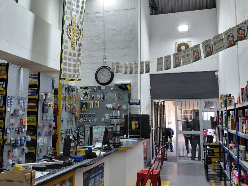 Commercial retail space featuring a service counter, extensive metal shelving for inventory, high ceilings, and a secure entrance gate.