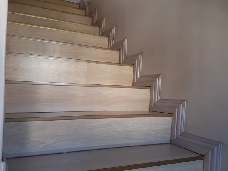 A clean, well-maintained staircase featuring light wood-look treads and a modern metal handrail.