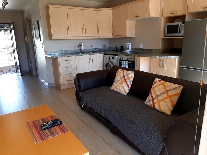 Open-plan living area featuring a functional kitchen with light wood cabinetry, granite countertops, and integrated appliances, leading to an outdoor balcony area.