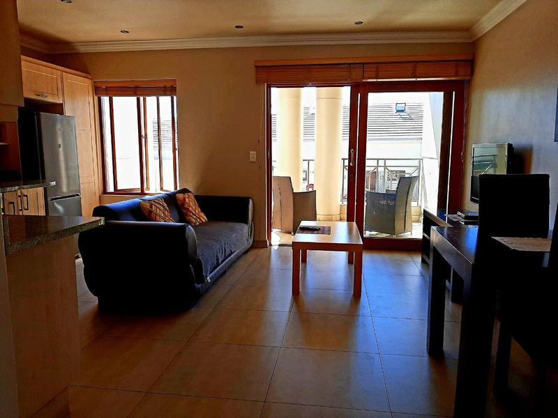 Open-plan living area featuring tiled floors, integrated kitchen cabinetry, and sliding glass doors leading to a private balcony.