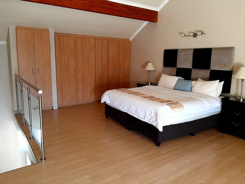 Spacious loft-style bedroom featuring vaulted ceilings, exposed timber beams, extensive built-in cabinetry, and a modern glass balustrade overlooking the lower level.