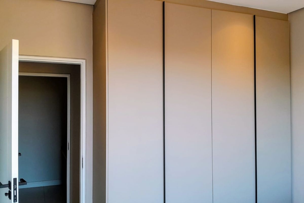 A clean, modern bedroom interior featuring floor-to-ceiling built-in cupboards with minimalist black trim and a neutral color palette.