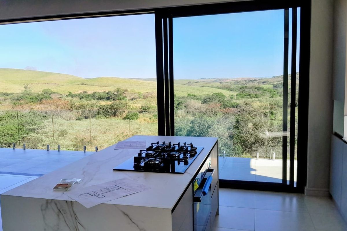 Modern kitchen featuring a central island with a built-in gas hob and oven, opening onto a patio with expansive rural views.
