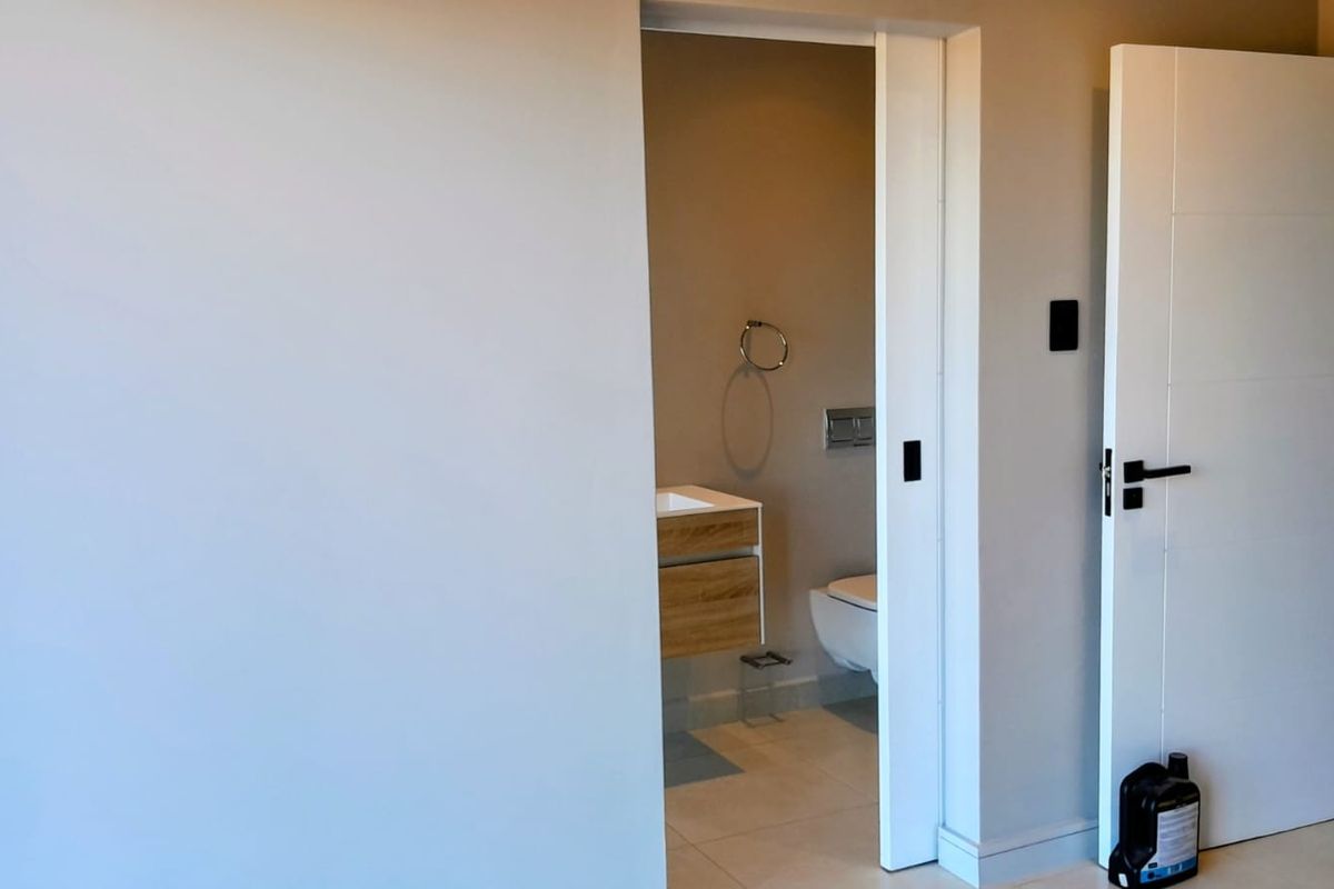 A modern, minimalist bathroom featuring a wall-mounted vanity and wall-hung toilet, accessed through a clean white doorway.