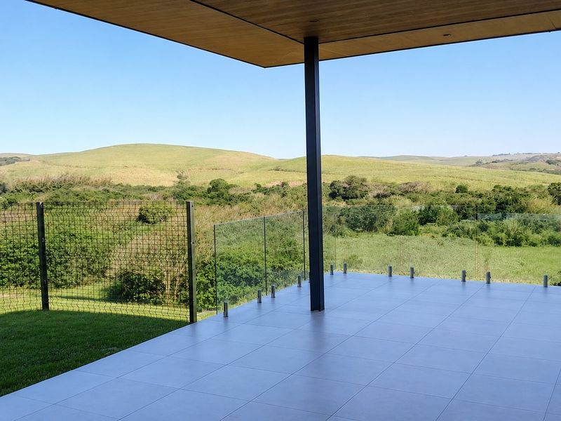 A modern covered patio featuring large format floor tiles, a sleek glass balustrade, and expansive views of the surrounding landscape.
