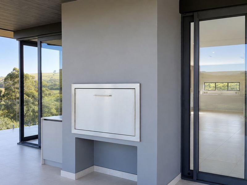 A modern covered balcony featuring a built-in braai, sleek tiled flooring, and expansive sliding glass doors offering scenic views of the surrounding landscape.
