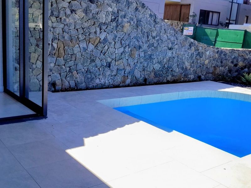 Modern outdoor pool area featuring a tiled patio, stone cladding feature wall, and large sliding glass doors leading into the home.
