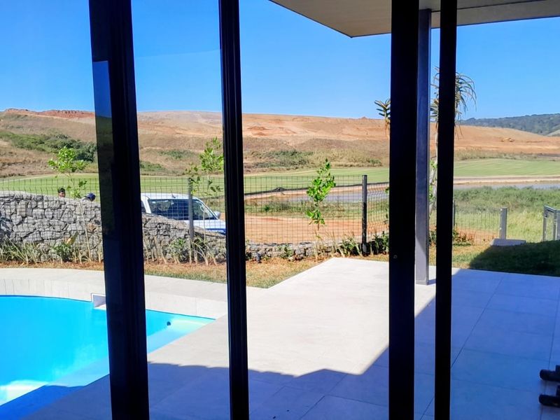 A covered patio area featuring tiled flooring and direct access to a swimming pool, overlooking a landscaped estate and natural landscape.