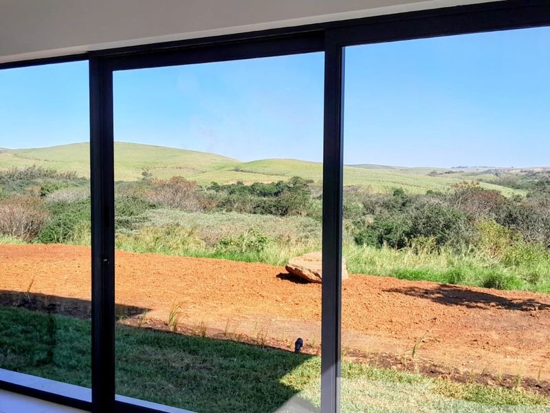 A view from inside looking out through large sliding glass doors towards a natural landscape with rolling hills.