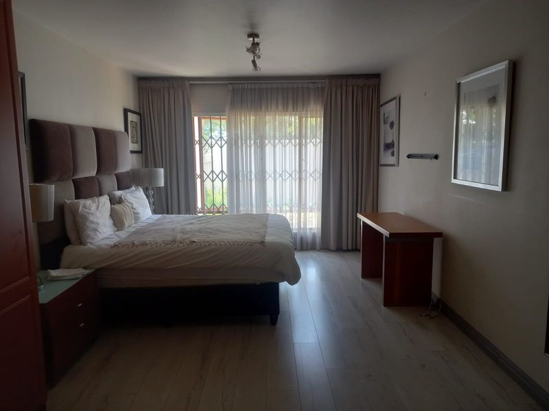A well-lit bedroom featuring light-toned laminate flooring, neutral walls, and a security gate leading to an outdoor area.