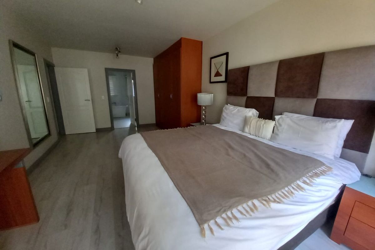 Spacious bedroom featuring laminate flooring, a large built-in wardrobe, and an upholstered headboard, with an adjoining bathroom visible through the doorway.