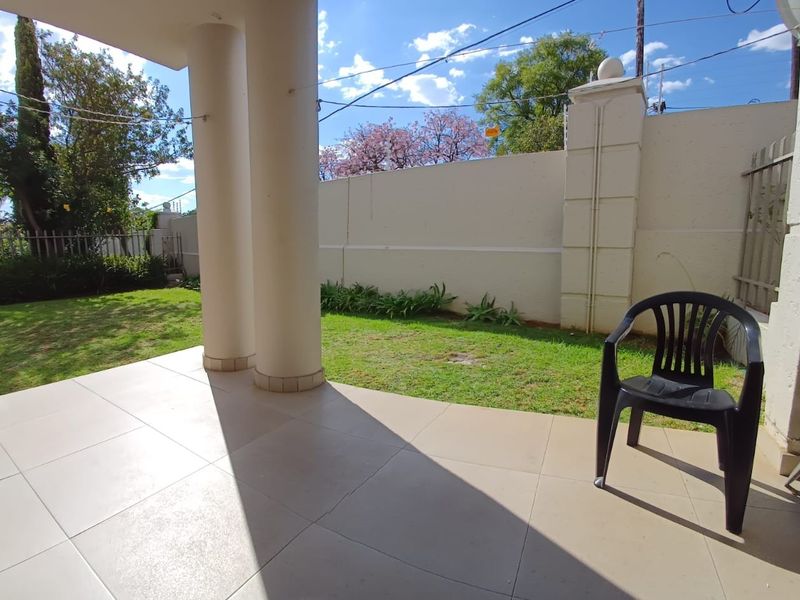 A covered patio area featuring tiled flooring and structural columns, overlooking a private garden space enclosed by a perimeter boundary wall.