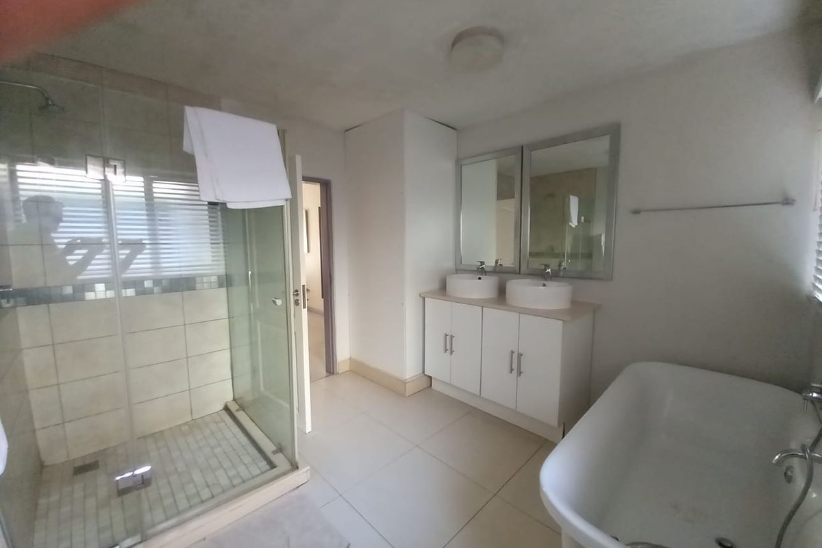 Spacious bathroom featuring a glass-enclosed shower, a double vanity with vessel sinks, and a freestanding bathtub with neutral floor tiling.