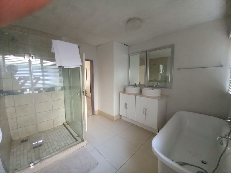 Spacious bathroom featuring a glass-enclosed shower, a double vanity with vessel sinks, and a freestanding bathtub with neutral floor tiling.