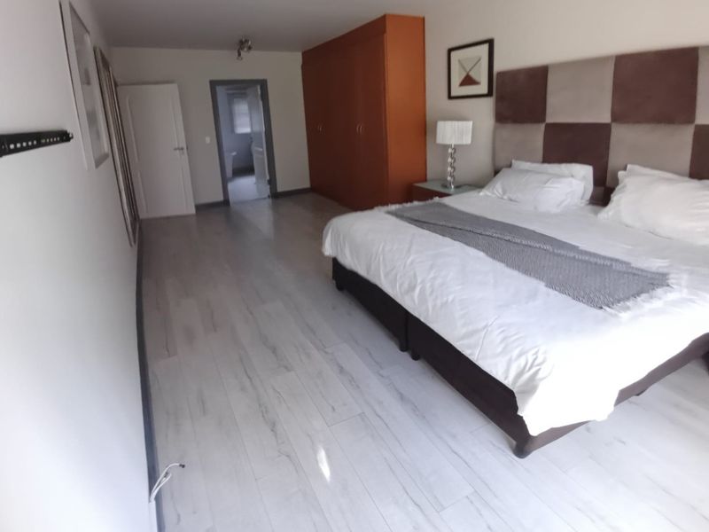 Spacious bedroom featuring light-toned laminate flooring, a large built-in wardrobe, and a neutral color palette with direct access to an adjoining room.
